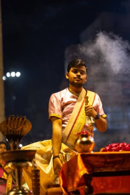 Varanasi, Uttar Pradesh, Hindistan - 3 Mart 2023: Ganga aarti, Dashashwamedh ghat geleneksel elbise ve Hindu ayinleri ile kutsal nehir ganges akşam aarti performans genç rahip portresi