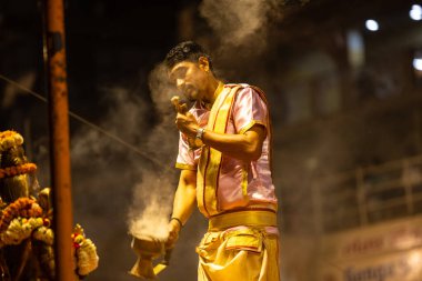 Varanasi, Uttar Pradesh, Hindistan - 3 Mart 2023: Ganga aarti, Dashashwamedh ghat geleneksel elbise ve Hindu ayinleri ile kutsal nehir ganges akşam aarti performans genç rahip portresi