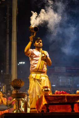 Varanasi, Uttar Pradesh, Hindistan - 3 Mart 2023: Ganga aarti, Dashashwamedh ghat geleneksel elbise ve Hindu ayinleri ile kutsal nehir ganges akşam aarti performans genç rahip portresi