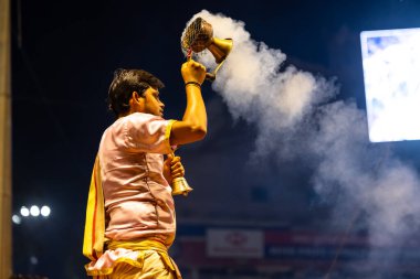 Varanasi, Uttar Pradesh, Hindistan - 3 Mart 2023: Ganga aarti, Dashashwamedh ghat geleneksel elbise ve Hindu ayinleri ile kutsal nehir ganges akşam aarti performans genç rahip portresi
