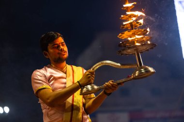 Varanasi, Uttar Pradesh, Hindistan - 3 Mart 2023: Ganga aarti, Dashashwamedh ghat geleneksel elbise ve Hindu ayinleri ile kutsal nehir ganges akşam aarti performans genç rahip portresi
