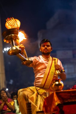 Varanasi, Uttar Pradesh, Hindistan - 3 Mart 2023: Ganga aarti, Dashashwamedh ghat geleneksel elbise ve Hindu ayinleri ile kutsal nehir ganges akşam aarti performans genç rahip portresi