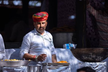Faridabad, Haryana, Hindistan - Şubat 04 2023: Geleneksel elbise içindeki rajasthani erkek şefin portresi ve renkli türban Surajkund panayırında rajasthani yemeği hazırlıyor