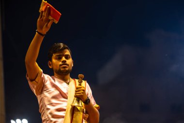 Varanasi, Uttar Pradesh, Hindistan - 3 Mart 2023: Ganga aarti, Dashashwamedh ghat geleneksel elbise ve Hindu ayinleri ile kutsal nehir ganges akşam aarti performans genç rahip portresi