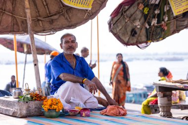 Varanasi, Uttar Pradesh, Hindistan - 05 Mart 2023: Varanasi şehrinde geleneksel elbise giyen varanasi çetelerinin yakınlarındaki Kedar ghat 'ta oturan kimliği belirsiz Hintli erkek rahibin portresi.