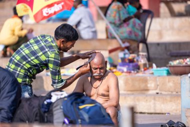 Varanasi, Uttar Pradesh, Hindistan - 05 Mart 2023: Sokak berberi Varanasi 'de Hindu ayinlerinin bir parçası olarak çetelerin yanında saç ve sakal traşı oluyor.