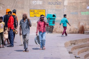 Varanasi, Uttar Pradesh, Hindistan - 05 Mart 2023: İş yerinde tanışan Hintli erkek işçi grubu, nehir keneviri yakınlarındaki ghat üzerinde inşaat sahasına ekipmanlarıyla yürüyorlar