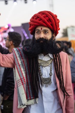 Bikaner, Rajasthan, Hindistan - 14 Ocak 2023: Bikaner deve festivalinde geleneksel Rajasthani elbisesi, mücevheri ve türban giyen sakallı ve bıyıklı bir rajasthani erkeğinin portresi.
