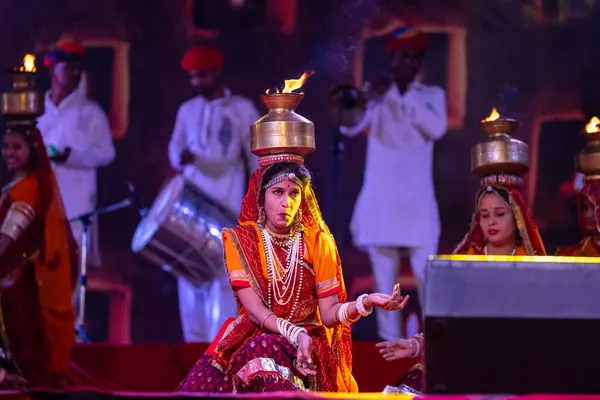 stock image Pushkar, Rajasthan, India - November 05, 2022: An female artists performing rajasthani folk dance Ghoomar in traditional colorful dresses and metal pots with fire in Pushkar fair. Selective focus.