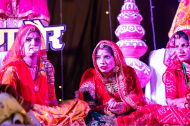 Bikaner, Rajasthan, Hindistan - 13 Ocak 2023: Geleneksel renkli rajashani kıyafetleri içinde güzel bir kadın grubu ve deve festivali sırasında sahnede kültürel gangaur pooja gösterisi.