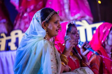 Bikaner, Rajasthan, India - January 13 2023: Group of beautiful female of bikaner in traditional colourful rajashani clothes and performing cultural gangaur pooja on stage during the camel festival. clipart