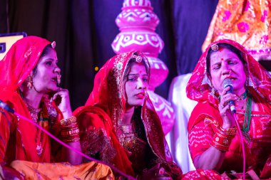 Bikaner, Rajasthan, Hindistan - 13 Ocak 2023: Geleneksel renkli rajashani kıyafetleri içinde güzel bir kadın grubu ve deve festivali sırasında sahnede kültürel gangaur pooja gösterisi.