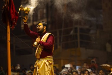 Varanasi, Uttar Pradesh, Hindistan - 18 Ocak 2024: Ganga aarti, Genç erkek rahibin portresi Dashashwamedh ghat 'ta kutsal nehir ganges akşam aarti gösterisi Hindu ayinleri ile geleneksel elbise.