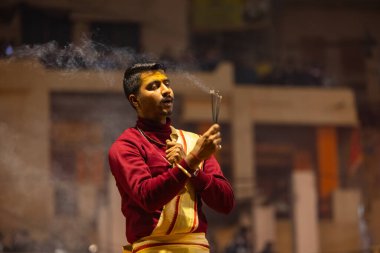 Varanasi, Uttar Pradesh, Hindistan - 18 Ocak 2024: Ganga aarti, Genç erkek rahibin portresi Dashashwamedh ghat 'ta kutsal nehir ganges akşam aarti gösterisi Hindu ayinleri ile geleneksel elbise.