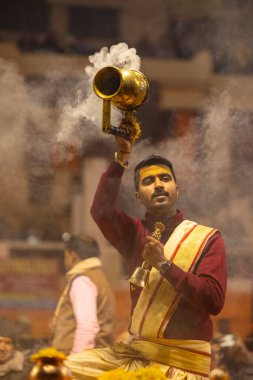 Varanasi, Uttar Pradesh, Hindistan - 18 Ocak 2024: Ganga aarti, Genç erkek rahibin portresi Dashashwamedh ghat 'ta kutsal nehir ganges akşam aarti gösterisi Hindu ayinleri ile geleneksel elbise.