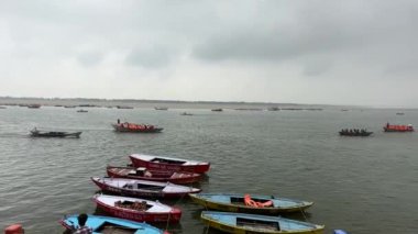 Varanasi, Uttar Pradesh, Hindistan - 22 Mart 2024: Varanasi 'deki nehir çetelerinde yüzen ahşap botlar bulutlu gökyüzü altında.
