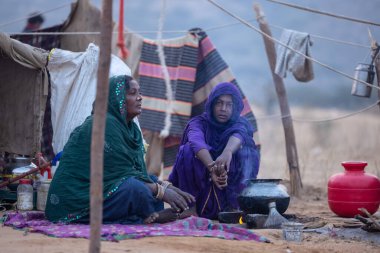 Puşkar, Rajasthan, Hindistan - 24 Kasım 2023: Pushkar Deve Fuarı sırasında Hindistan 'da kış sabahı yerde oturan kadınların portresi. 