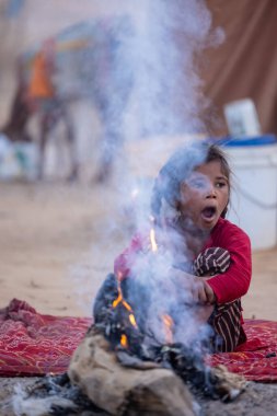 Puşkar, Rajasthan, Hindistan - 24 Kasım 2023: Sisli kış sabahında sisli bir deve fuarı sırasında yerde oturan terk edilmiş genç mülteci kız portresi.