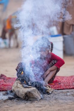 Puşkar, Rajasthan, Hindistan - 24 Kasım 2023: Sisli kış sabahında sisli bir deve fuarı sırasında yerde oturan terk edilmiş genç mülteci kız portresi.