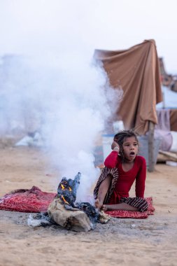 Puşkar, Rajasthan, Hindistan - 24 Kasım 2023: Sisli kış sabahında sisli bir deve fuarı sırasında yerde oturan terk edilmiş genç mülteci kız portresi.