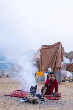 Puşkar, Rajasthan, Hindistan - 24 Kasım 2023: Sisli kış sabahında sisli bir deve fuarı sırasında yerde oturan terk edilmiş genç mülteci kız portresi.