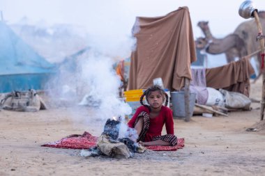 Puşkar, Rajasthan, Hindistan - 24 Kasım 2023: Sisli kış sabahında sisli bir deve fuarı sırasında yerde oturan terk edilmiş genç mülteci kız portresi.