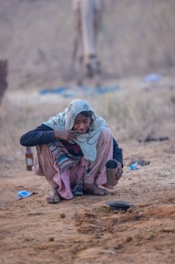 Puşkar, Rajasthan, Hindistan - 24 Kasım 2023: İtme kar deve fuarı sırasında kış sabahı yerde oturan etnik kıyafetli genç kadın portresi.