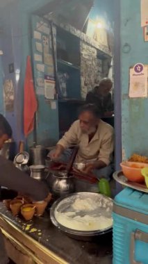 Varanasi, Uttar Pradesh, Hindistan - 21 Kasım 2022: Yaşlı adam Varanasi 'de bir dükkanda süt lor lassi hazırlıyor. Varanasi 'nin sokakları çok meşhurdur ve turistler buraya yemek yemeye gelir.. 