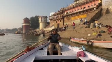 Varanasi, Uttar Pradesh, Hindistan - 21 Kasım 2022: Varanasi 'deki nehir çetelerinde elleri bağlı tahtadan bir tekneye binen kimliği belirsiz bir kayıkçının videosu.