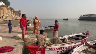 Varanasi, Uttar Pradesh, Hindistan - 21 Kasım 2022: Kutsal nehir çetelerinin kıyısında balıkçı ağı üzerinde çalışan bir grup balıkçı. Ghat 'a parkedilmiş ahşap tekneler.