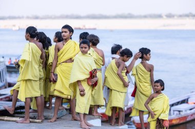 Varanasi, Uttar Pradesh, Hindistan - 05 Mart 2023: Ganj nehrinin kıyısında açık bir sınıfta çalışmak üzere duran gurukul 'un etnik sarı elbiseli genç erkek öğrencileri.