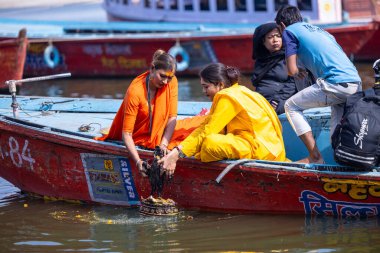 Varanasi, Uttar Pradesh, Hindistan - 05 Mart 2023: Bir grup dişi sadhvi, kutsal nehir çetelerinde ahşap bir tekneye biniyor