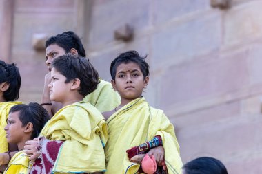 Varanasi, Uttar Pradesh, Hindistan - 5 Mart 2023: Gurukul 'un etnik sarı elbiseli genç erkek öğrencileri, kutsal nehir çetelerinin kıyılarında açık sınıftaki ghatlar üzerinde çalışmak üzere duruyorlar.