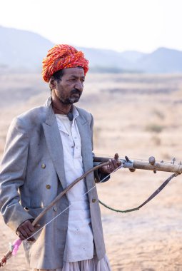 Puşkar, Rajasthan, Hindistan - 23 Kasım 2023: Rajasthani erkek bir ressamın portresi geleneksel rajasthani elbisesiyle kafasının üzerinde renkli türban ve mekânda müzik aleti Sarangi ile.