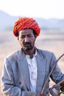 Puşkar, Rajasthan, Hindistan - 23 Kasım 2023: Rajasthani erkek bir ressamın portresi geleneksel rajasthani elbisesiyle kafasının üzerinde renkli türban ve mekânda müzik aleti Sarangi ile.