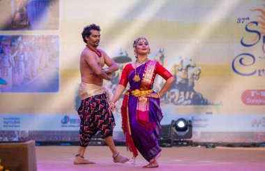 Faridabad, Haryana, Hindistan - 17 Şubat 2024: Erkek ve kadın Güney Hintli sanatçılar etnik renkli kostümler içinde surajkund sanatları fuarı sırasında sahnede klasik dans kuchipudi performansı sergiliyorlar.