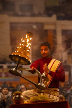 Varanasi, Uttar Pradesh, India - January 18, 2024: Ganga aarti, Portrait of young male priest performing holy river Ganges evening aarti at Dashashwamedh Ghat in traditional dress with hindu rituals. clipart