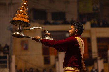 Varanasi, Uttar Pradesh, Hindistan - 18 Ocak 2024: Ganga aarti, Dashashwamedh Ghat geleneksel elbise ve Hindu ayinleri ile Ganj nehri akşam ayini yapan genç rahip portresi.