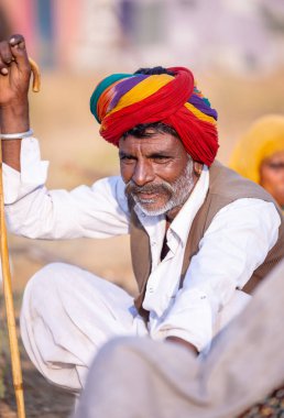 Puşkar, Rajasthan, Hindistan - 23 Kasım 2023: Rajasthan 'lı beyaz elbiseli bir adamın portresi ve Pushkar deve fuarı sırasında çöl panayırında renkli bir türban.