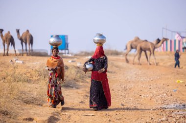 Puşkar, Rajasthan, Hindistan - 24 Kasım 2023: Pushkar deve panayırında yürürken kafalarında çelik su kapları taşıyan iki kadın.