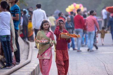 Gaziabad, Uttar Pradesh, Hindistan - 19 Kasım 2023: Nehir kıyısına doğru yürüyen bir grup Hintli aile ile birlikte etnik renkli giysiler içinde Chhas puja ayinlerini gerçekleştirmek için.