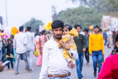 Gaziabad, Uttar Pradesh, Hindistan - 19 Kasım 2023: Nehir kıyısına doğru yürüyen bir grup Hintli aile ile birlikte etnik renkli giysiler içinde Chhas puja ayinlerini gerçekleştirmek için.