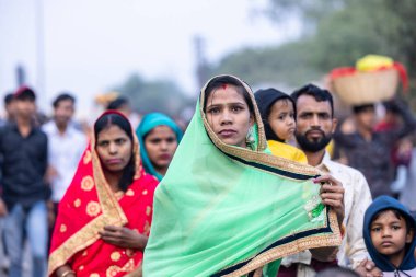Gaziabad, Uttar Pradesh, Hindistan - 19 Kasım 2023: Nehir kıyısına doğru yürüyen bir grup Hintli aile ile birlikte etnik renkli giysiler içinde Chhas puja ayinlerini gerçekleştirmek için.