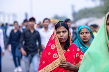 Gaziabad, Uttar Pradesh, Hindistan - 19 Kasım 2023: Nehir kıyısına doğru yürüyen bir grup Hintli aile ile birlikte etnik renkli giysiler içinde Chhas puja ayinlerini gerçekleştirmek için.