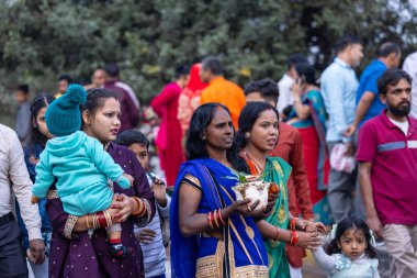 Gaziabad, Uttar Pradesh, Hindistan - 19 Kasım 2023: Nehir kıyısına doğru yürüyen bir grup Hintli aile ile birlikte etnik renkli giysiler içinde Chhas puja ayinlerini gerçekleştirmek için.