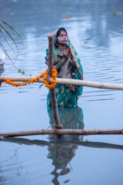 Gaziabad, Uttar Pradesh, Hindistan - 19 Kasım 2023: Chhas Puja, Hintli kadın dindar Chhas puja 'nın portresi gün batımında güneş tanrısı güneşe ibadet etmek için nehirde durarak ritüellerini gerçekleştiriyor..