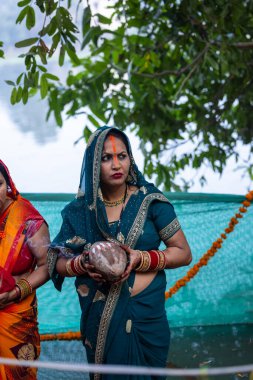 Ghaziabad, Uttar Pradesh, India - November 19 2023: Chhath Puja, Portrait of indian hindu female devotees performing rituals of chhath puja with standing in river to worship lord sun during sunset. clipart