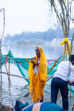 Gaziabad, Uttar Pradesh, Hindistan - 19 Kasım 2023: Chhas Puja, Hintli Hintli erkek dindar portresi Chhas puja ritüellerini gerçekleştiriyor ve gün batımında Lord Sun 'a ibadet etmek için nehirde duruyor..