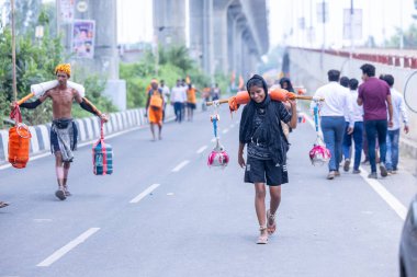 Ghaziabad, Uttar Pradesh, India - July 31 2024: Portrait of Hindu female pilgrims performing Kanwar Yatra barefoot during Sawan Shivratri and carrying holy ganga water to worship Hindu god Shiva with rituals. clipart