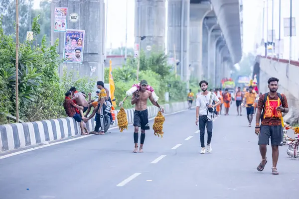 Gaziabad, Uttar Pradesh, Hindistan - 31 Temmuz 2024: Sawan Shivratri sırasında çıplak ayakla Kanwar Yatra 'yı seslendiren Hindu hacıların portresi ve Hindu tanrısı Shiva' ya ibadet etmek için kutsal Ganga suyu taşımak.